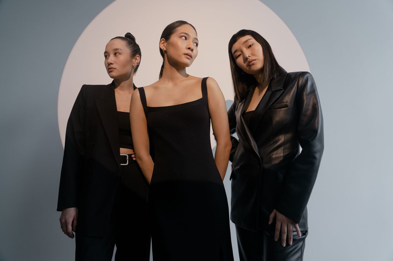 services-04 Three women in sleek outfits pose confidently under artistic lighting for a modern portrait.