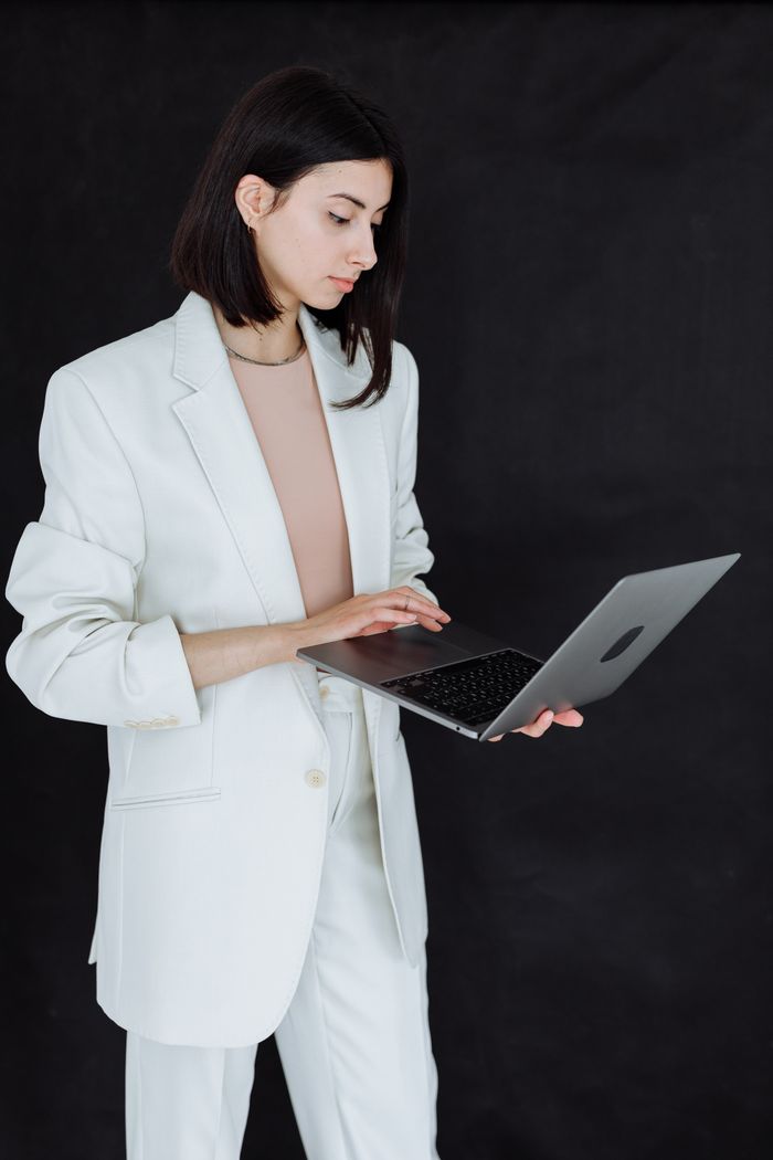 services-02 Professional woman in a white blazer using a laptop against a dark background.
